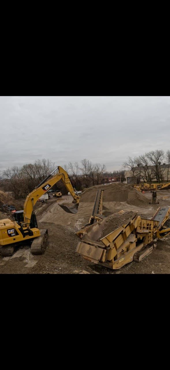 CAT 320 excavator feeding a mobile screening plant beside processed aggregate stockpiles